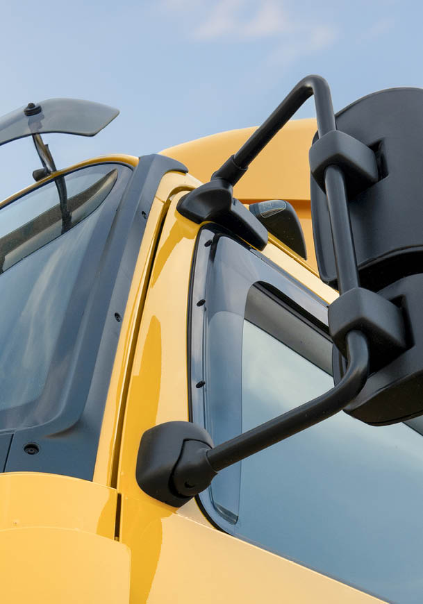 Close-up view of the side mirror and window of a yellow truck against a blue sky. Description generated by AI