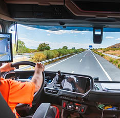 A person wearing glasses, a black beanie, and a high-visibility jacket is sitting in the driver's seat of a vehicle, smiling and giving a thumbs-up gesture. Description generated by AI