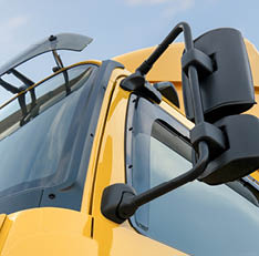 Close-up view of the side mirror and windshield area of a yellow truck cab against a blue sky. Description generated by AI