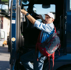 Senior truck driver with backpack exiting his truck after a long trip