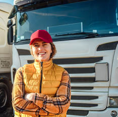 Portrait of a smiling female truck driver standing in front of a truck vehicle in the parking lot. Transportation service
