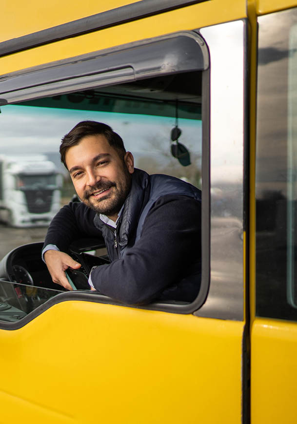 A person with short hair and a beard is smiling and leaning out of the window of a yellow vehicle. Description generated by AI
